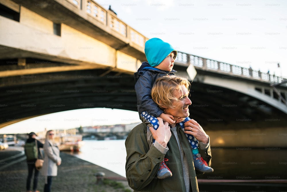 Un jeune père donne à son fils en bas âge un tour de ferroutage debout à l’extérieur au bord de la rivière en ville.