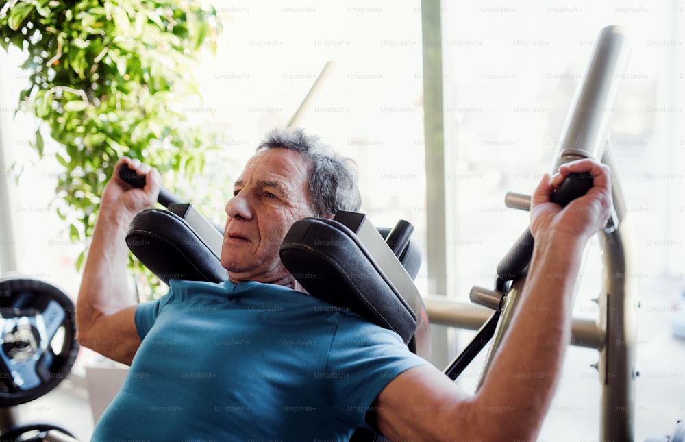Un uomo anziano concentrato che fa esercizio di allenamento di forza in palestra.