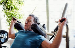 Un hombre mayor concentrado haciendo ejercicio de entrenamiento de fuerza en el gimnasio.