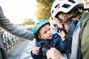 자전거 헬멧을 쓴 작은 유아 소년과 도시의 야외에서 알아볼 수없는 젊은 부모.