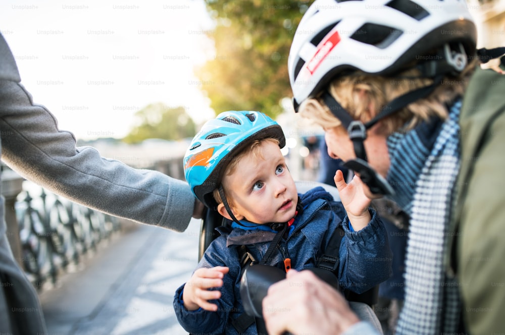 Un piccolo bambino con casco da bicicletta e giovani genitori irriconoscibili all'aperto in città.