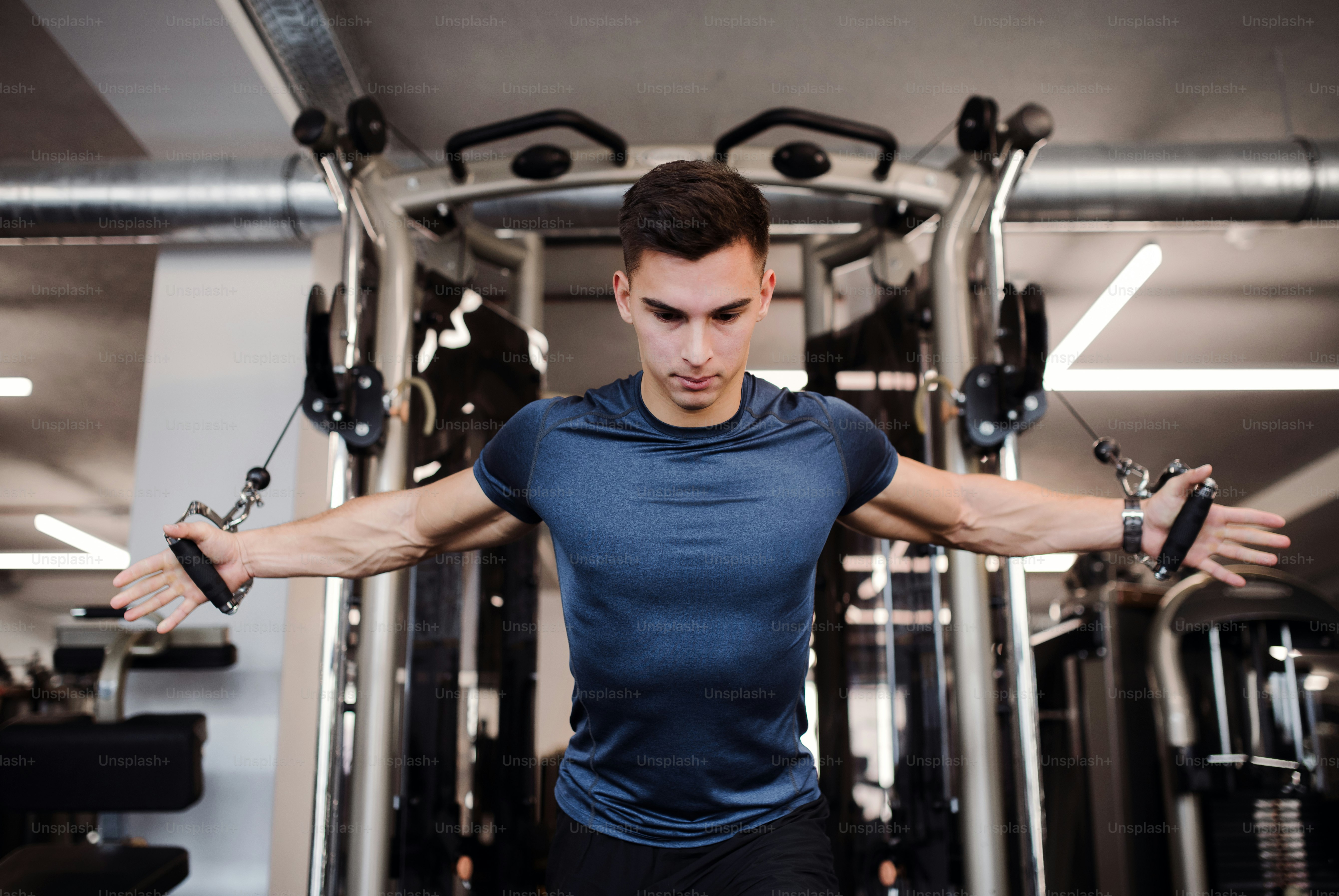 A concentrated young handsome man doing strength workout exercise in gym