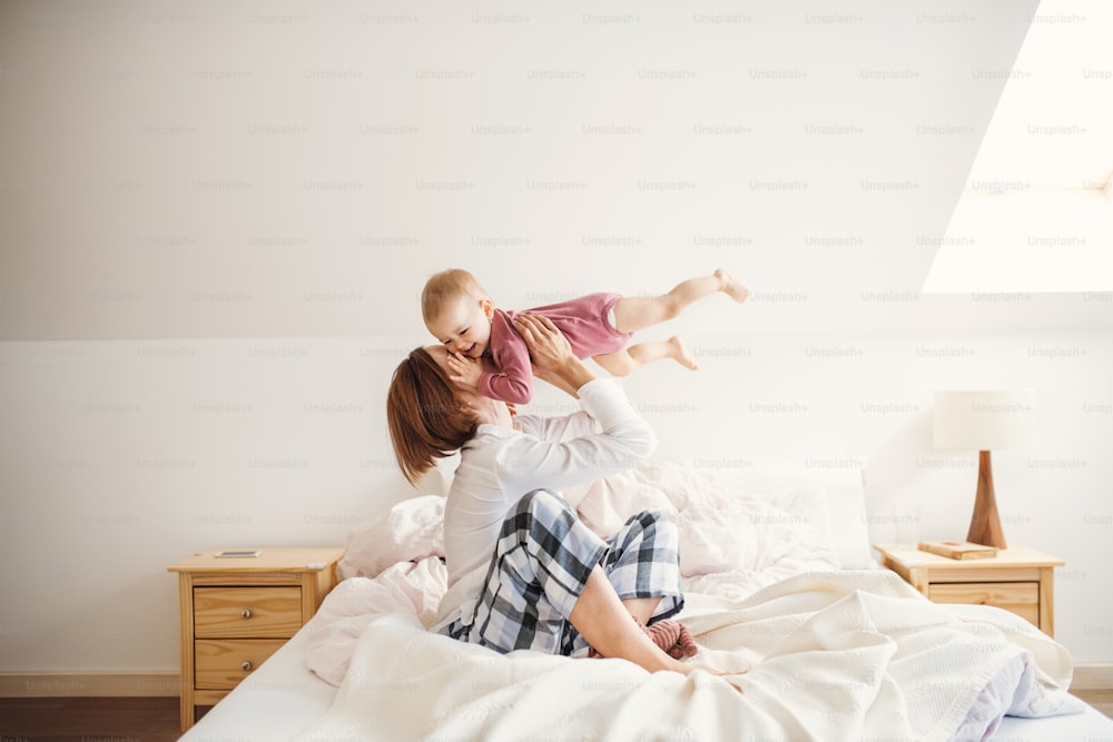 Una madre joven feliz con una hija pequeña sentada en la cama por la mañana, jugando.