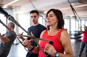 A group of cheerful seniors in gym with a young personal trainer doing exercise with TRX.