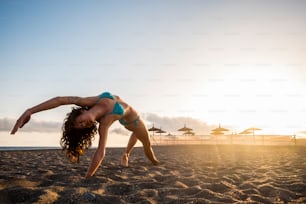Allenamento fitness di yoga e pilates in spiaggia per attraenti brunette che fanno esercizi - luce dorata del tramonto sullo sfondo - stile di vita sano per i giovani millennial - concetto di vita in forma all'aperto