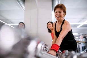 Eine Gruppe fröhlicher weiblicher Senioren im Fitnessstudio, die mit Hanteln trainieren.
