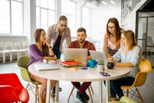 Team of a young coworkers dressed casually working together with laptops sitting at the round table in the office