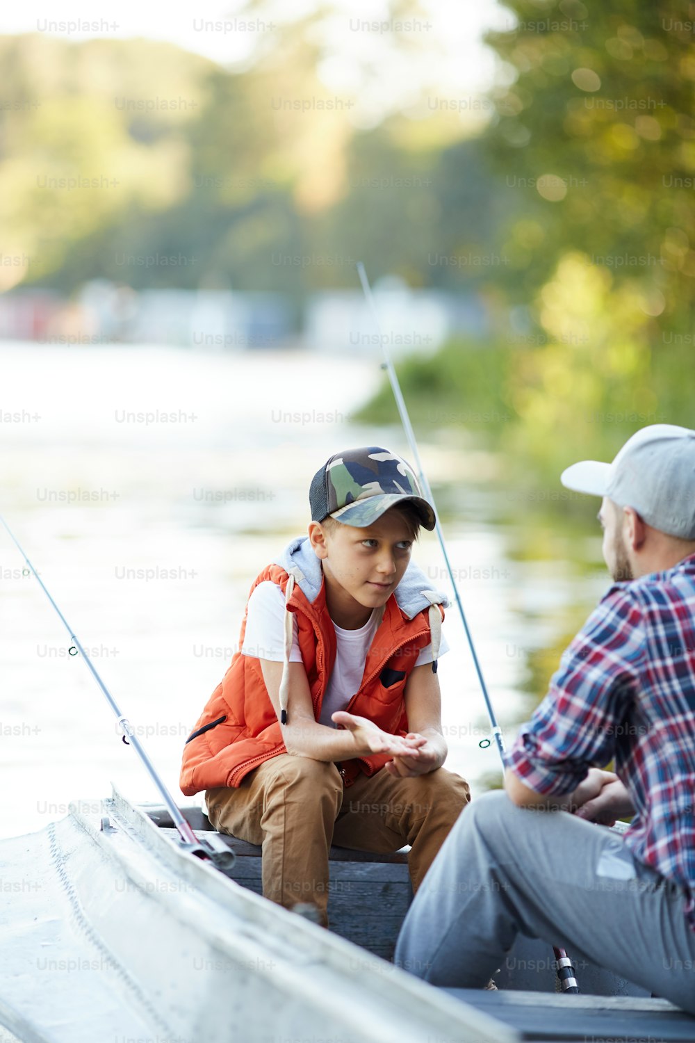 Kleiner Junge, der seinem Vater etwas fragt oder erklärt, während beide beim Angeln im Boot sitzen