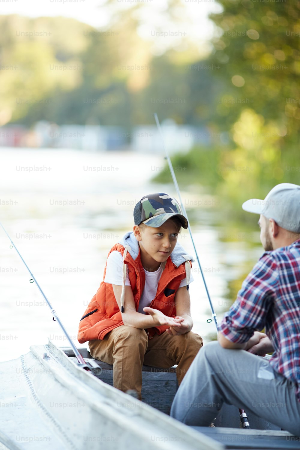 Little boy asking or explaining something to his dad while both sitting in boat during fishing