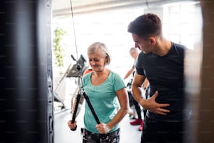 A cheerful female senior with a young trainer doing strength workout exercise in gym.