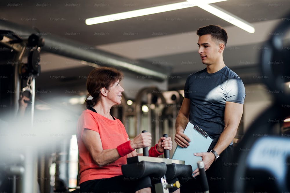 Uma idosa alegre com um jovem treinador fazendo exercícios de treino de força na academia.