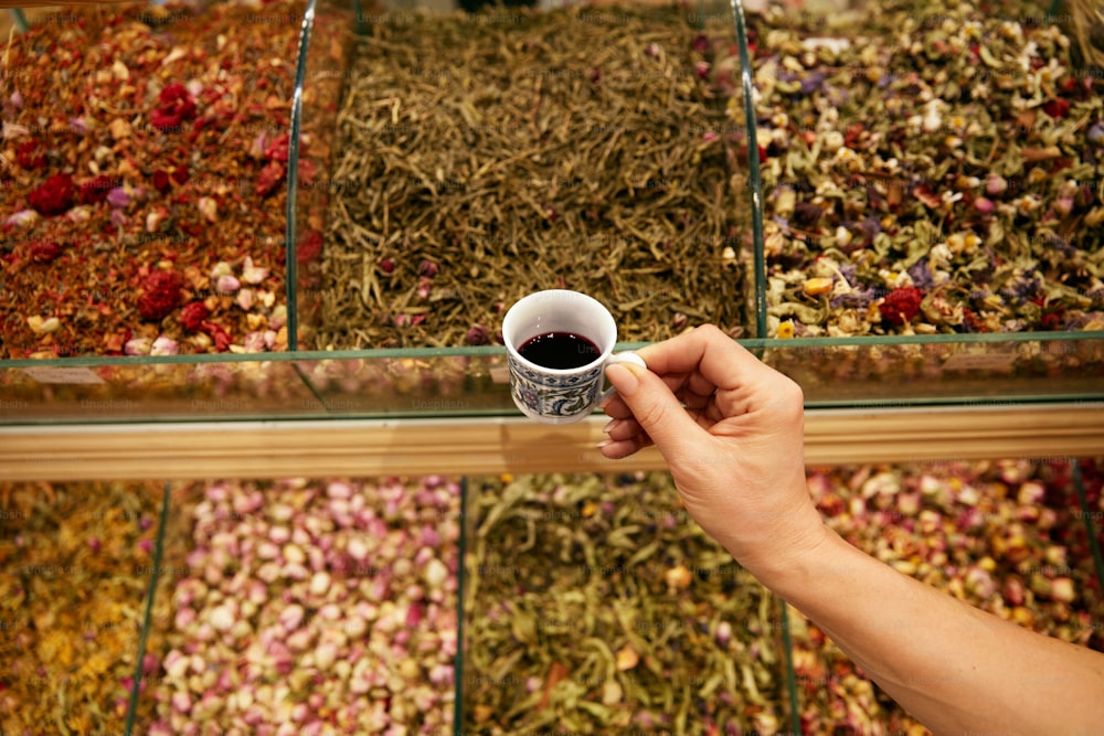 Hand mit Tasse türkischem rotem Tee in Ladennahaufnahme, Auswahl an Tee auf dem Hintergrund auf dem Markt. Hohe Auflösung