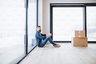 Un uomo maturo con scatole di cartone seduto sul pavimento, arredando una nuova casa. Un nuovo concetto di casa. Copia spazio.