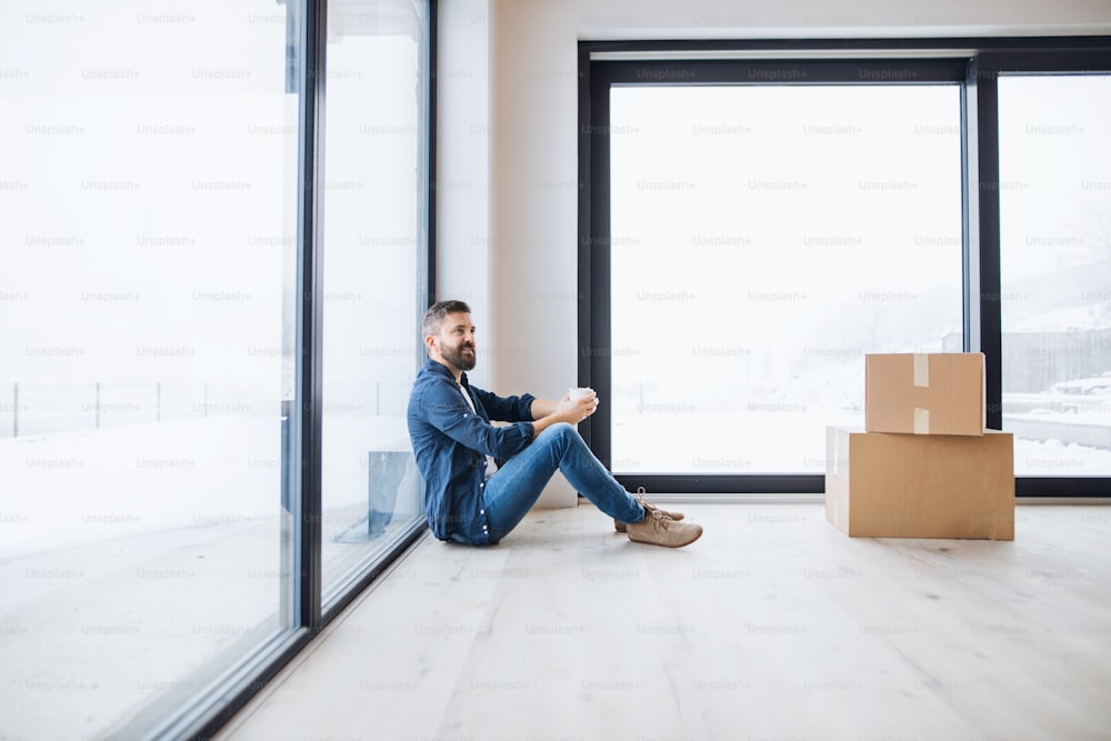Un hombre maduro con cajas de cartón sentado en el suelo, amueblando una casa nueva. Un nuevo concepto de hogar. Espacio de copia.