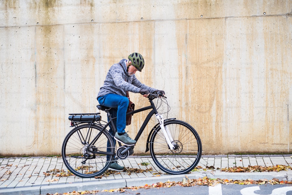 Homme âgé actif avec vélo électrique debout à l’extérieur en ville. Espace de copie.