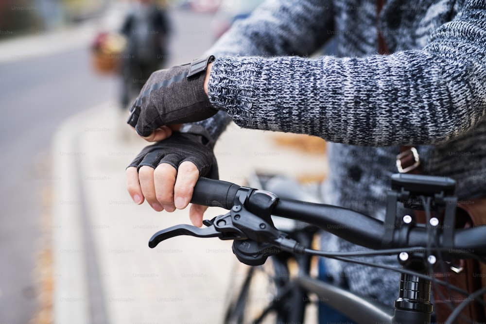 A close-up of a cyclist with electrobike putting on black gloves outdoors in town.