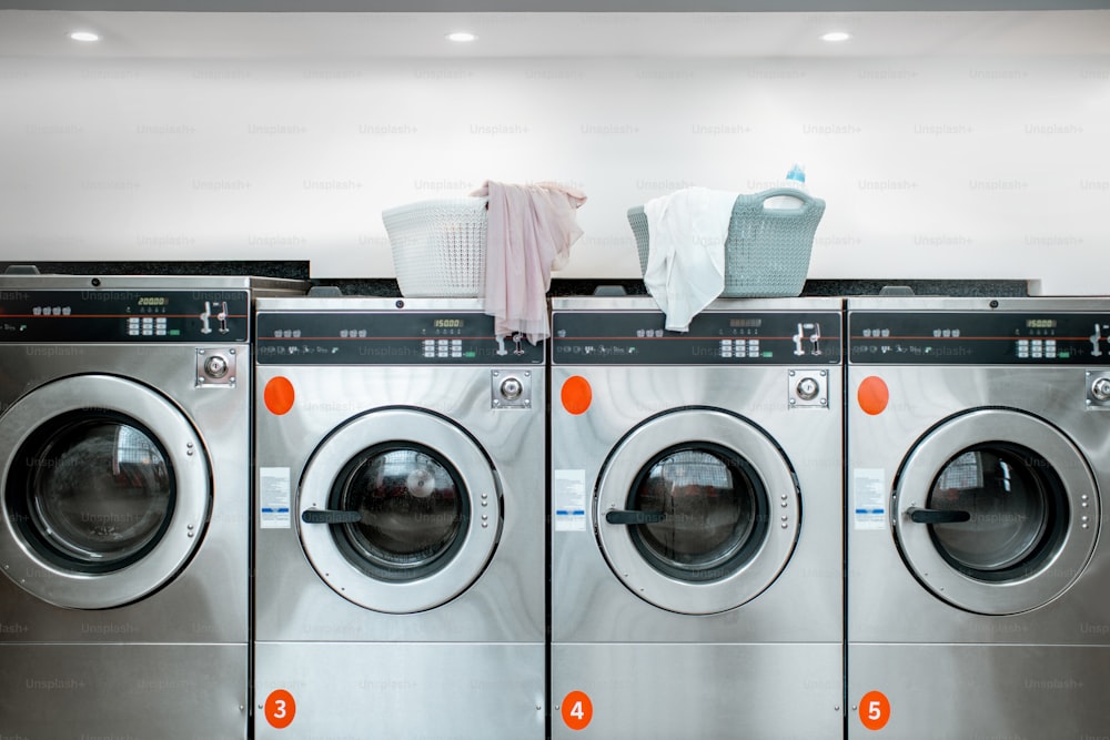 Lavatrici professionali con cestoni pieni di vestiti presso la lavanderia self-service