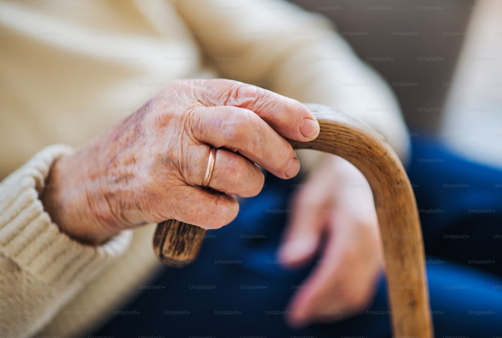 Um close-up de uma mulher idosa solitária sentada em uma poltrona em casa, segurando uma bengala.