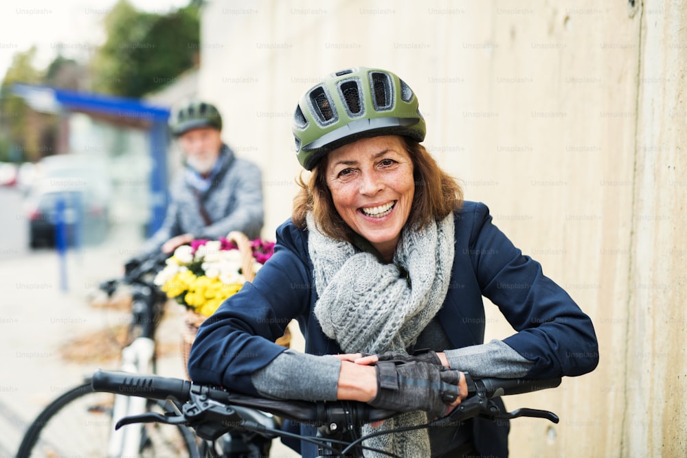 ヘルメットと電動自転車を身に着けたアクティブなシニアカップルが街の小道に立っている。