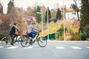 Couple de personnes âgées actives avec des vélos électriques à l’extérieur traversant une route en ville. Espace de copie.