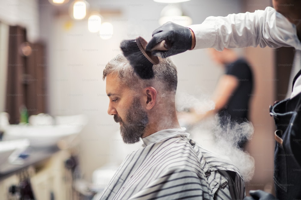 Cliente homem hipster bonito visitando haidresser e cabeleireiro em barbearia, fumando um cachimbo.