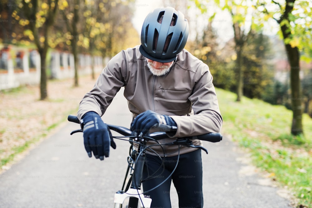 Um homem idoso ativo com capacete e eletrobicicleta ao ar livre em uma estrada na natureza.