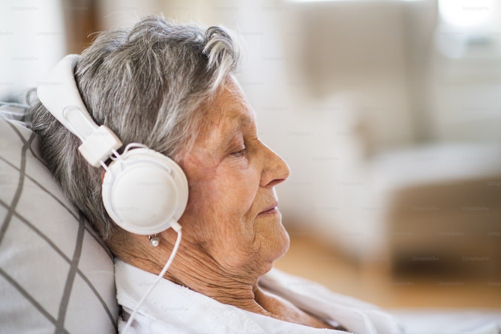Eine Nahaufnahme einer kranken älteren Frau mit Kopfhörern, die zu Hause oder im Krankenhaus im Bett liegt und Musik hört.