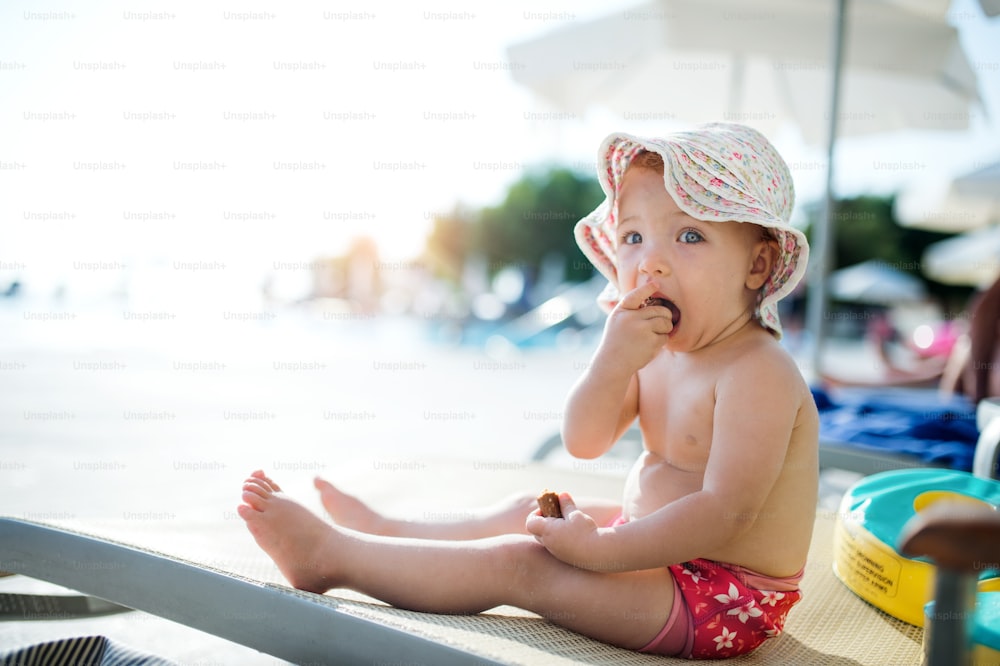 A cute small toddler girl sitting on beach on summer holiday. Copy space.