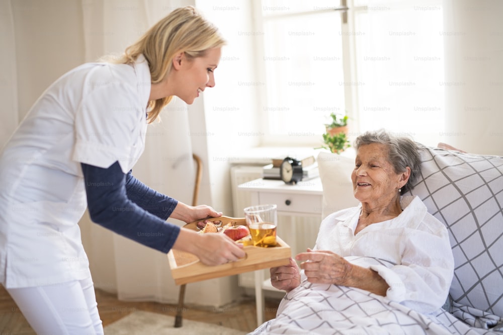 Un jeune visiteur de santé apporte le petit-déjeuner à une femme âgée malade allongée dans son lit à la maison.