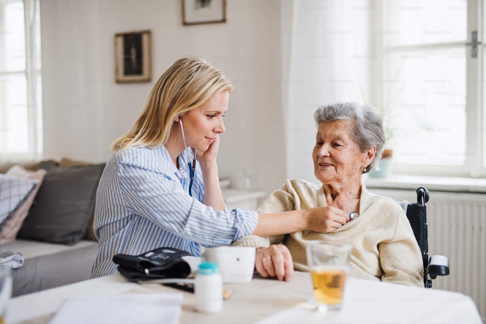 Ein junger Gesundheitsbesucher untersucht eine ältere Frau mit einem Stethoskop zu Hause.