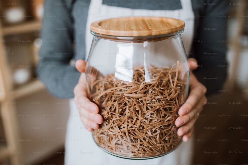 A midsection of a shop assistant in a zero waste shop, holding a jar with groceries. A close-up.