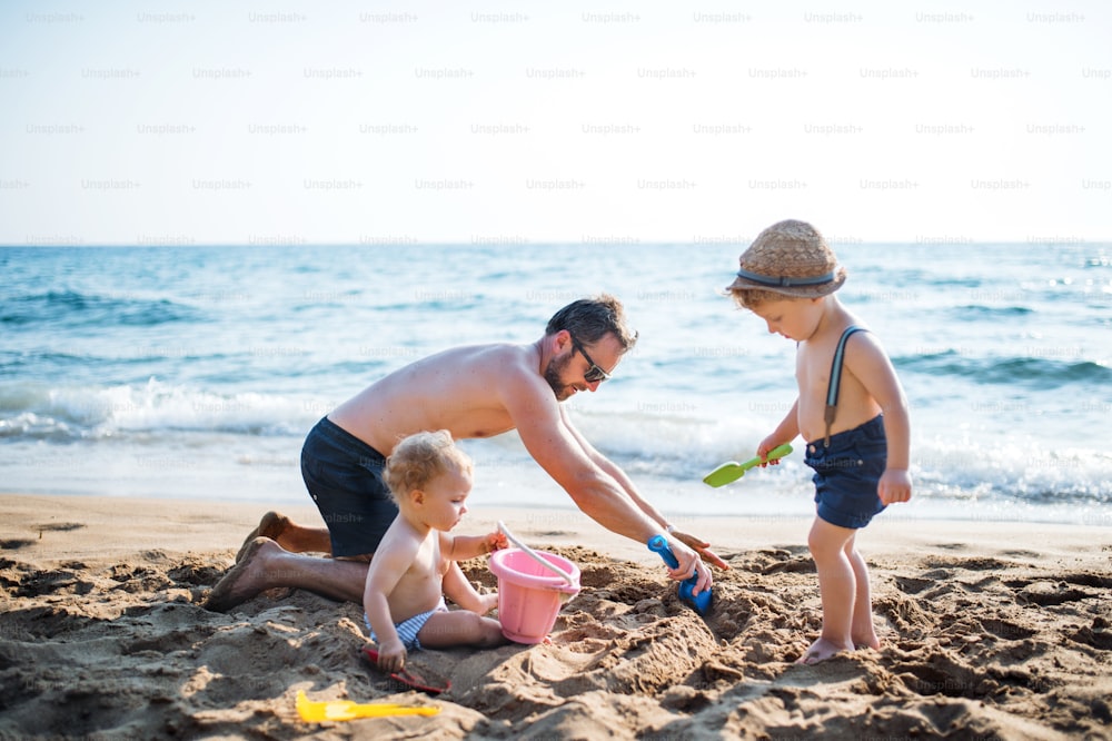 Ein reifer Vater mit zwei Kleinkindern, die in den Sommerferien mit Sand am Strand spielen.