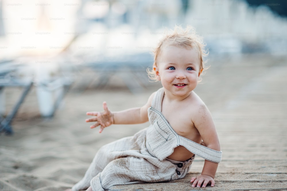 A cute small toddler girl sitting on beach on summer holiday. Copy space.