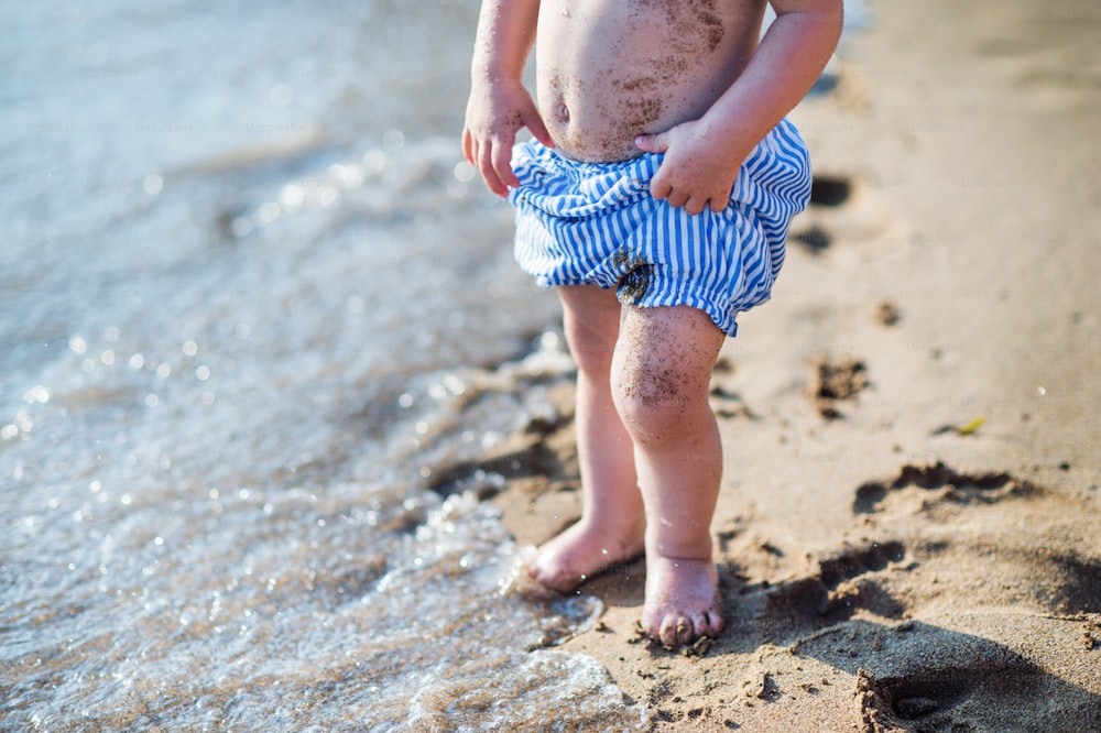 Una sezione centrale di una bambina piccola con pantaloncini che cammina sulla spiaggia di sabbia durante le vacanze estive.