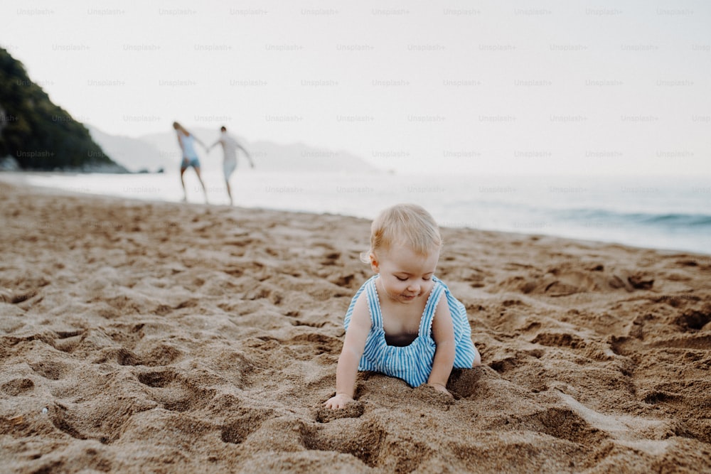 A small toddler girl playing in sand on beach on summer holiday. Copy space.