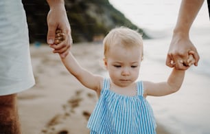 여름 휴가에 해변�을 걷고 있는 유아 딸과 함께 손을 잡고 있는 부모의 중간 부분.