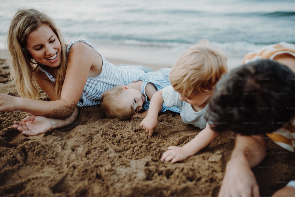 夏休みに砂浜に寝そべって遊んでいる2人の幼児の子供がいる家族。