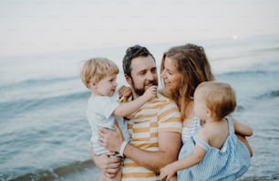 夏休みにビーチを歩く2人の幼児の子供を持つ家族。息子と娘を腕に抱える父と母。