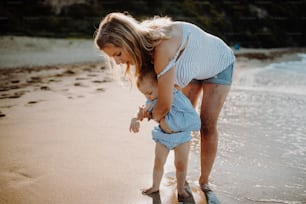 小さな幼い娘を連れた若い母親が夏休みにビーチを歩いている。