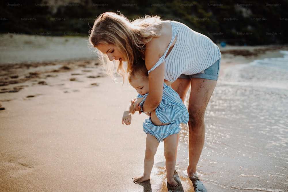 小さな幼い娘を連れた若い母親が夏休みにビーチを歩いている。
