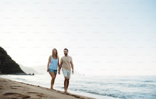 A cheerful man and woman walking on beach on summer holiday, holding hands. Copy space.