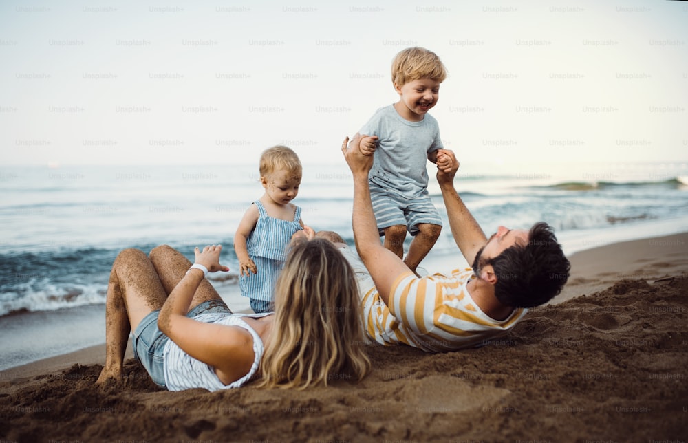 Una familia con dos niños pequeños tumbados en la playa de arena en vacaciones de verano, jugando.