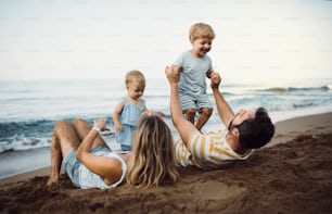 Uma família com duas crianças pequenas deitadas na praia de areia nas férias de verão, brincando.