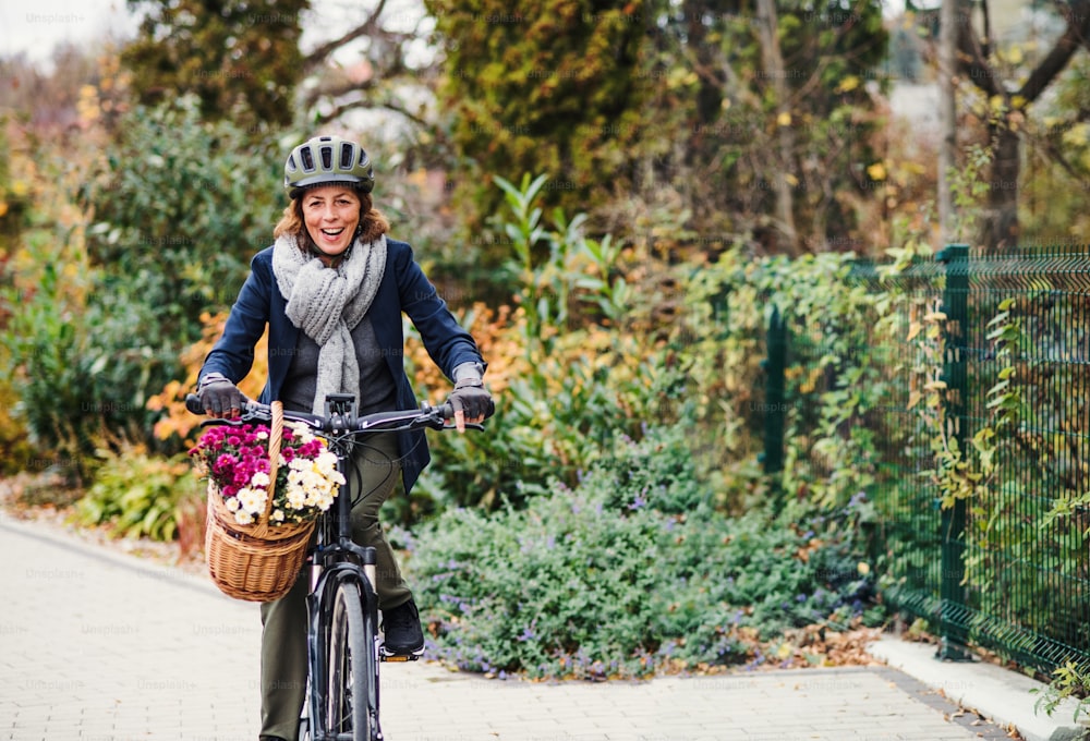 Une femme âgée active avec un casque et un vélo électrique qui fait du vélo à l’extérieur en ville. Espace de copie.
