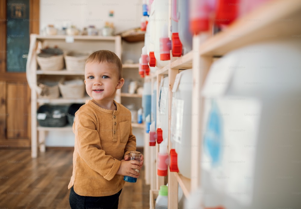 A cute small toddler boy standing by dispensers in zero waste shop.