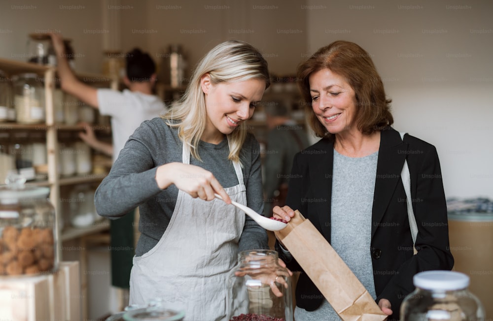 A young female shop assistant serving a senior customer in a zero-waste shop.