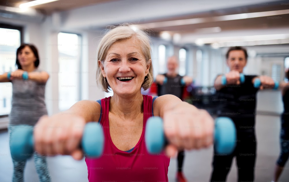 Un grupo de personas mayores alegres de pie en el gimnasio haciendo ejercicio con mancuernas.