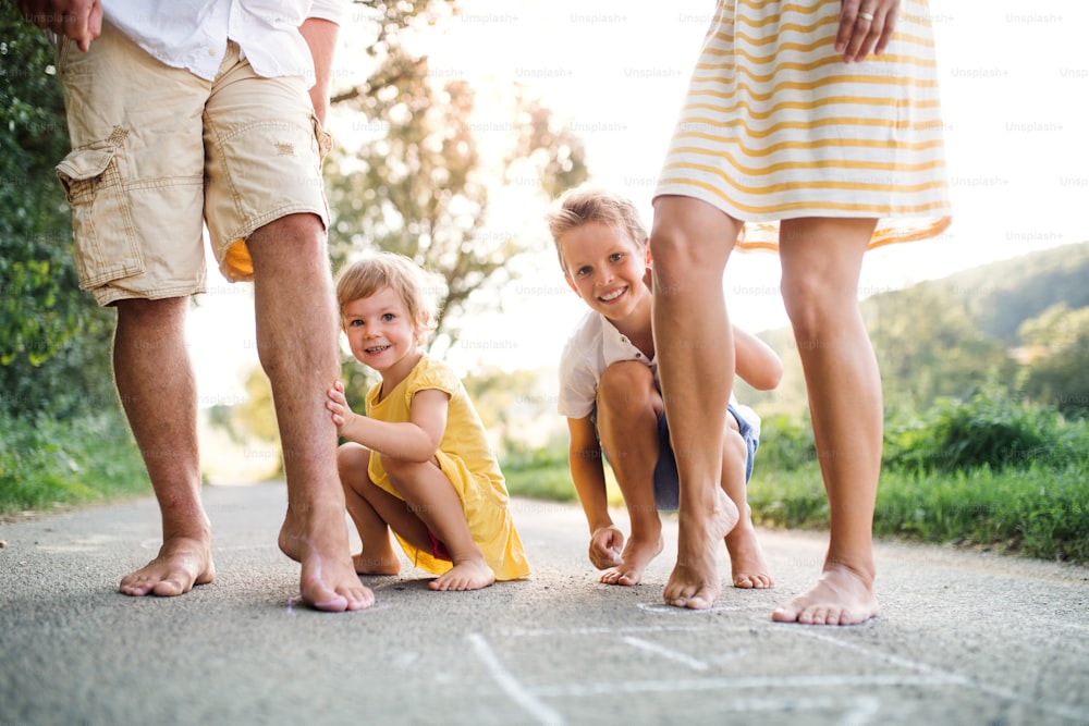 Una sección media de una familia joven con niños pequeños de pie descalzos en una carretera en verano en el campo.
