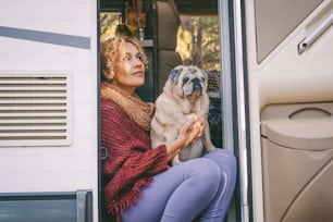 One woman sitting on the camper van door with old nice pug dog looking outside and enjoying relax and freedom. Female people living on a rv motorhome with animals and travel the world. Best friend