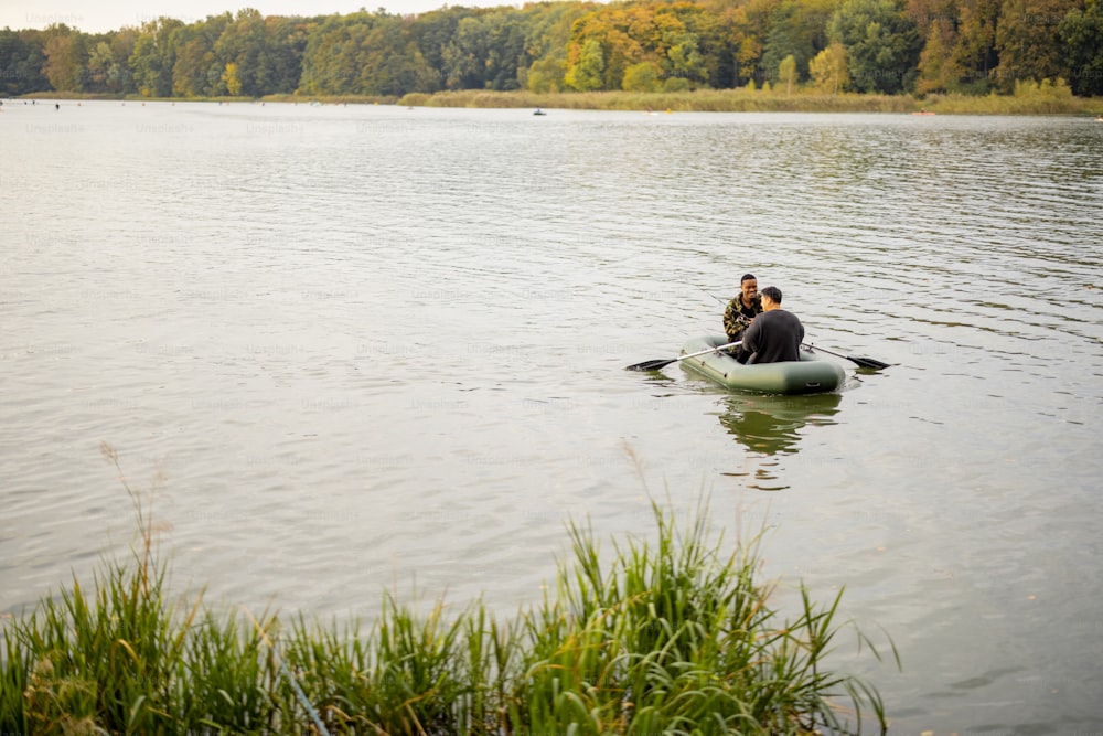 Multiracial male friends fishing with fishing rods on rubber boat in lake or river. Concept of rest and hobby in nature. Idea of friendship and spending time together. Wide view with copy space